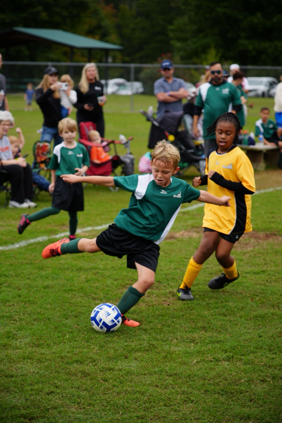 Children playing soccer while families watch from the sideline